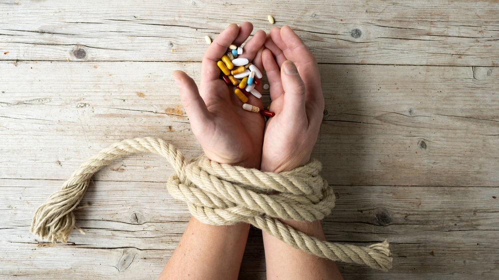 Mans hand tied by ropes holding drugs